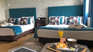 Ein Hotelzimmer mit zwei Betten, einem Nachttisch mit einem Tablet, einem Tablett mit Croissant und Saft sowie einer Wand mit Muster.