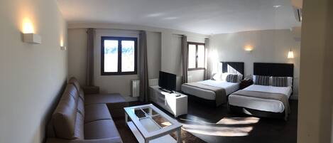 Habitación de hotel con sofá, dos camas, televisión y ventana con cortinas.