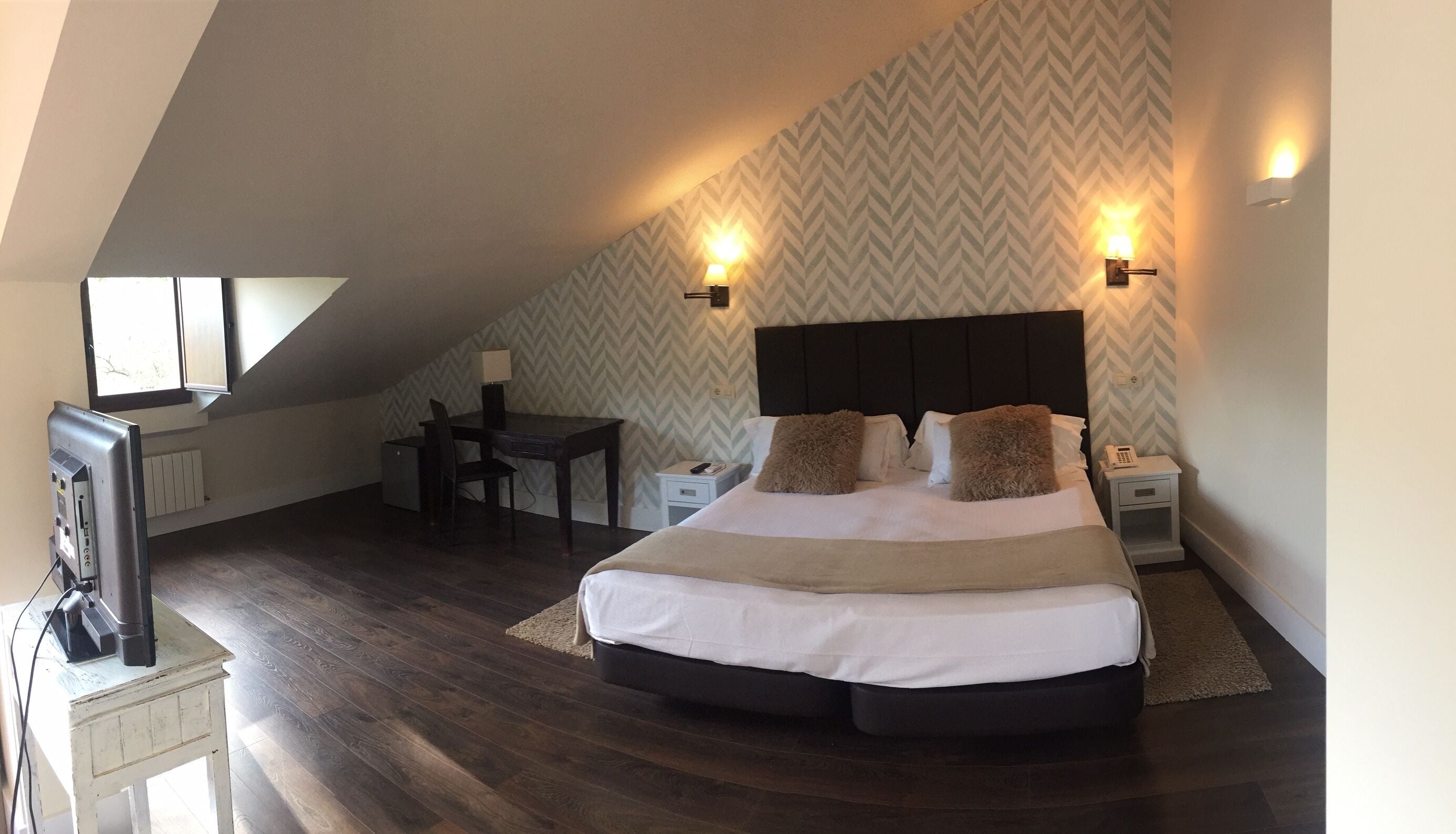 Un dormitorio con cama, mesitas de noche, escritorio y televisor.