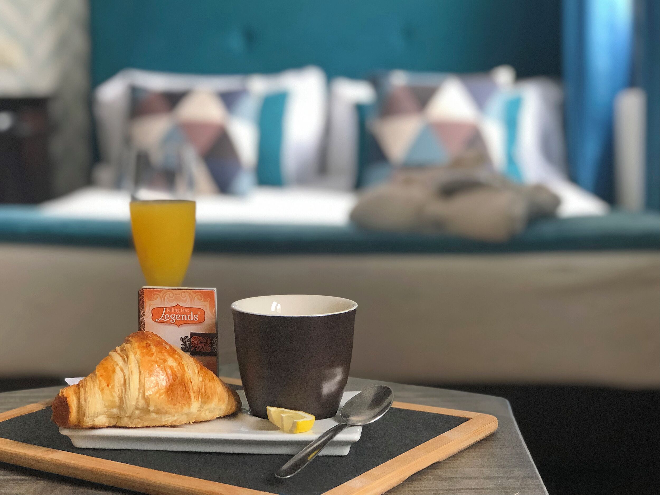 A breakfast setup with a croissant, a mug, a glass of orange juice, and a lemon wedge on a tray.