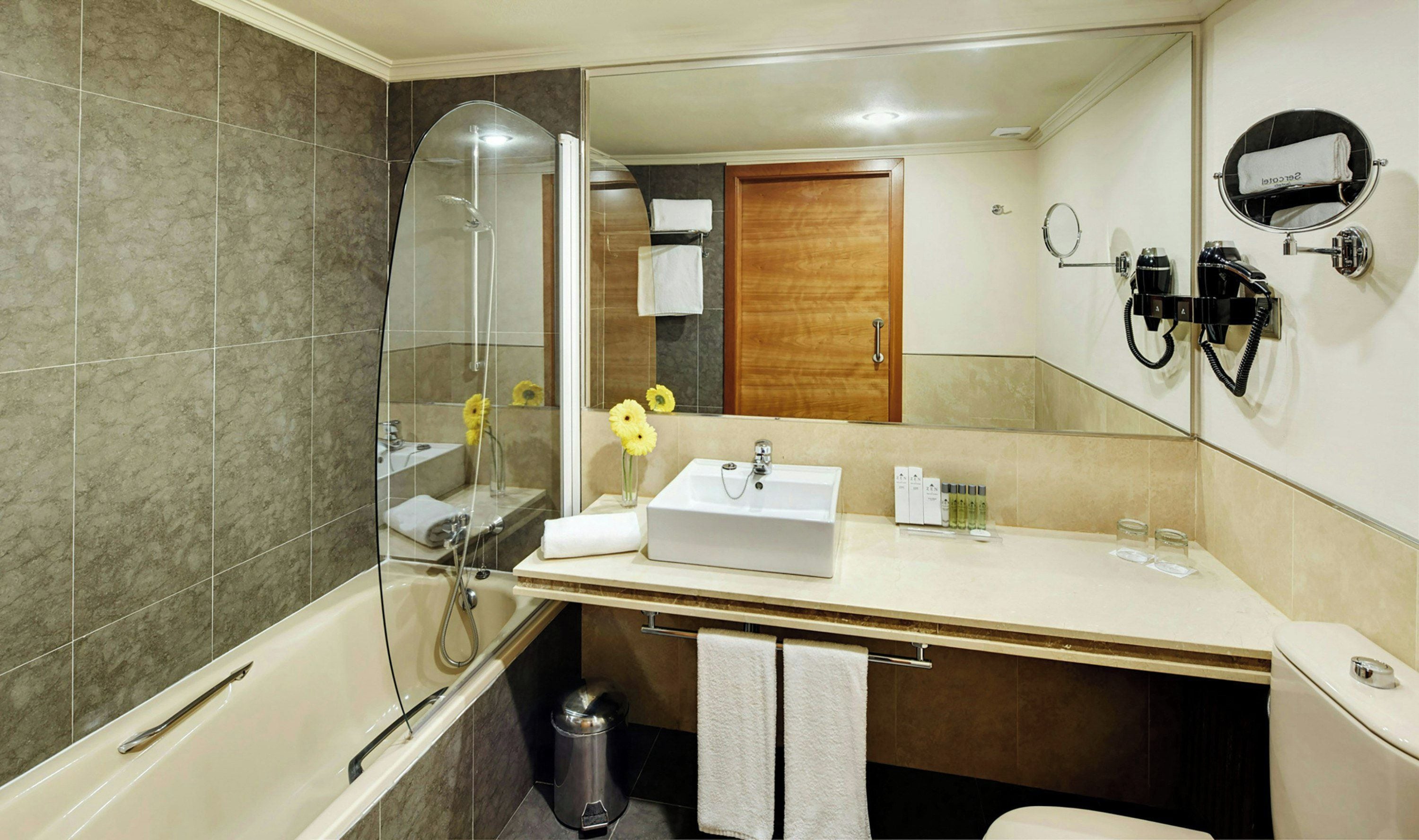 A modern bathroom with a glass-enclosed shower, a sink with toiletries, and a mirror with a hairdryer.