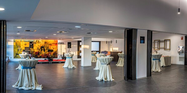 A spacious hall with round tables covered in white tablecloths and blue sashes, a stage with musical equipment, and a large abstract painting on the wall. - Sercotel Gran Hotel Zurbarán (Badajoz)