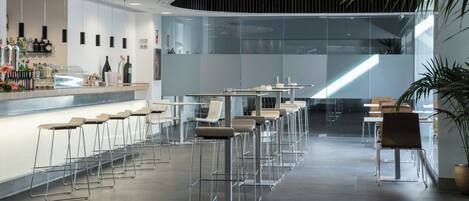 A modern bar area with high stools, a counter with bottles, and a glass partition.