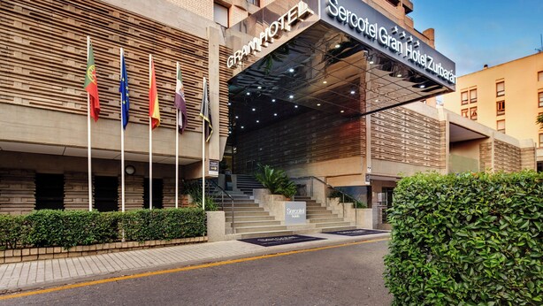 Fachada moderna de un hotel, con varias banderas y una escalera que conduce a la entrada.