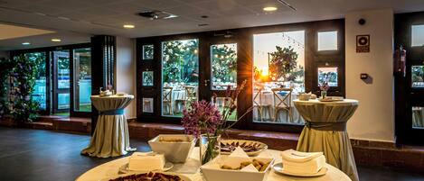 A banquet hall with round tables, a buffet setup, and large windows with natural light.