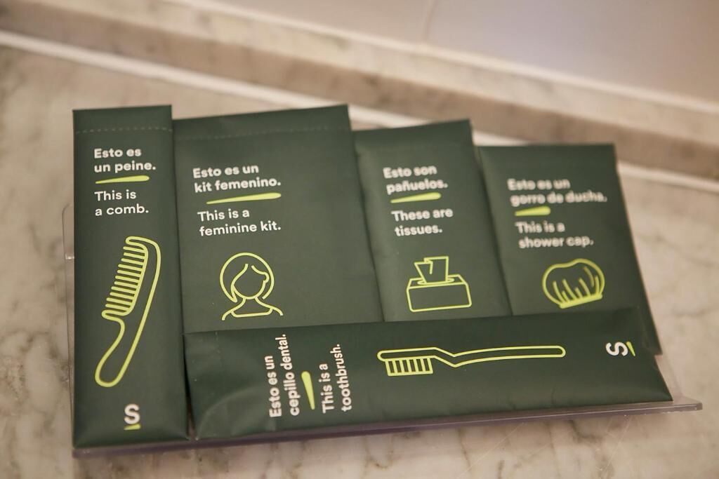 A set of four green boxes with text and icons, each labeled with a different item: comb, feminine kit, tissues, and shower cap.