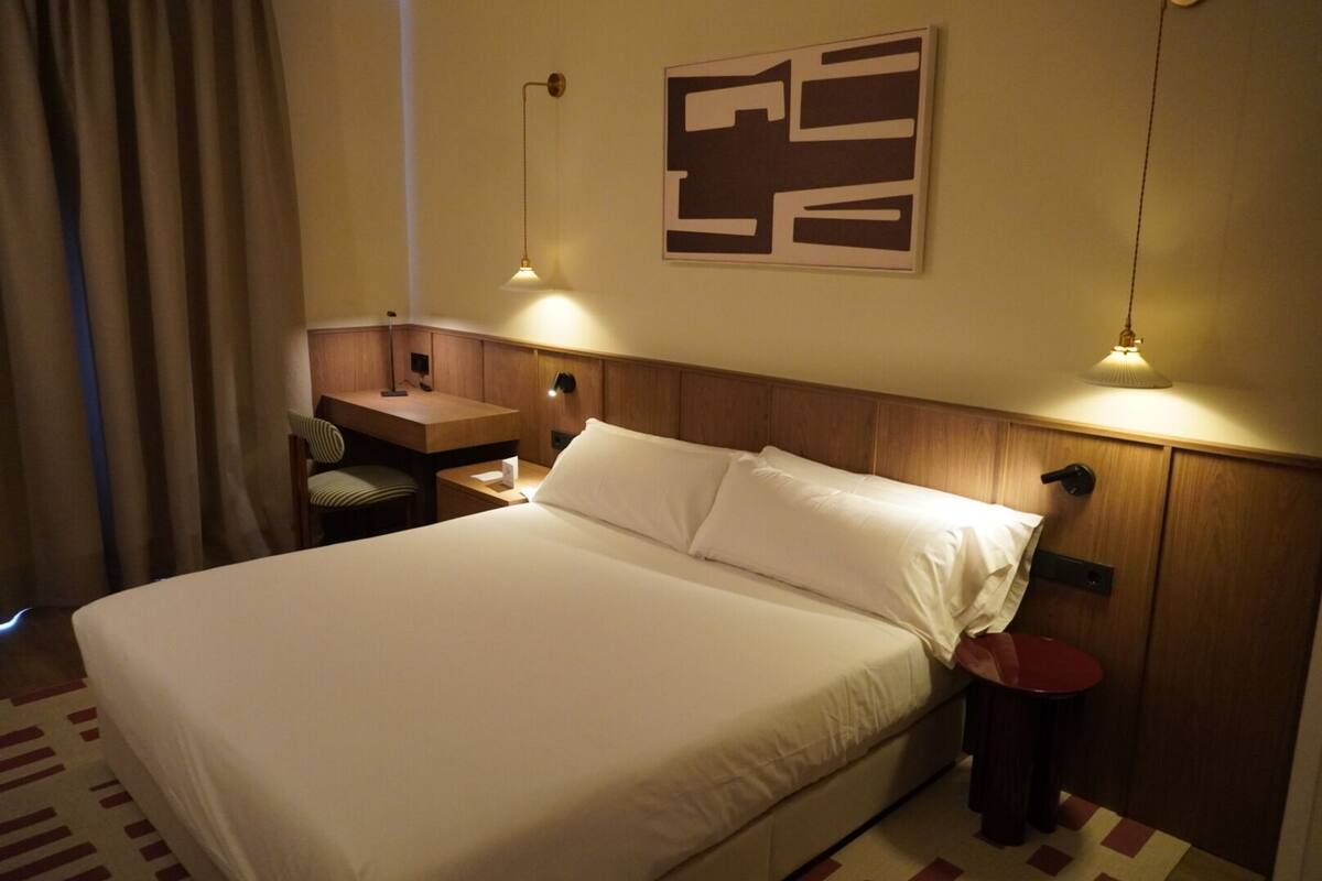 A hotel room with a bed, a desk, a chair, and two bedside lamps.