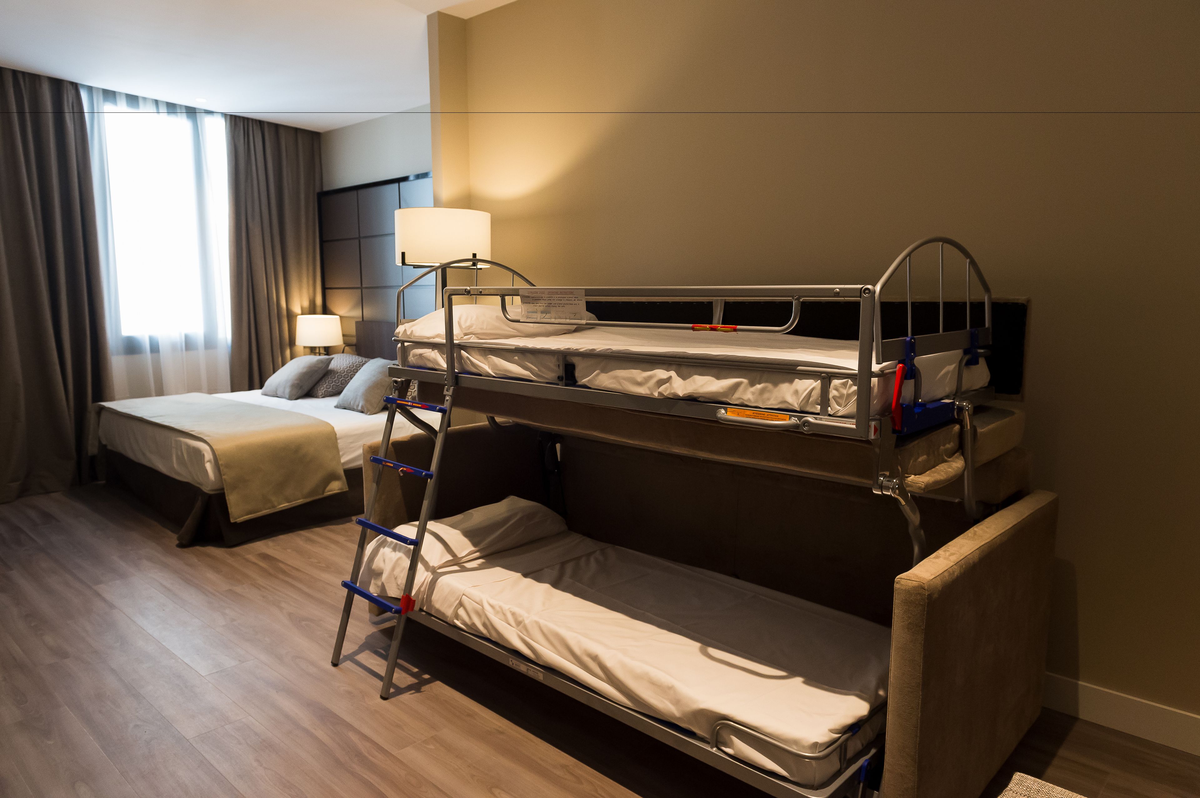 Een hotelkamer met twee bedden, een nachtkastje met een lamp en een raam met gordijnen.