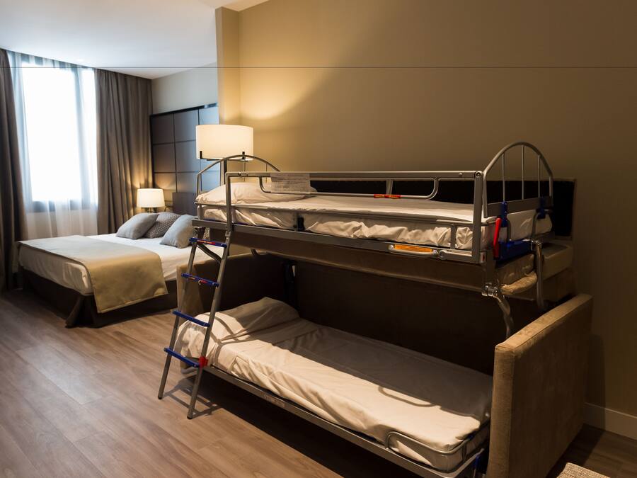Habitación de hotel con dos camas, una mesita de noche con lámpara y una ventana con cortinas.