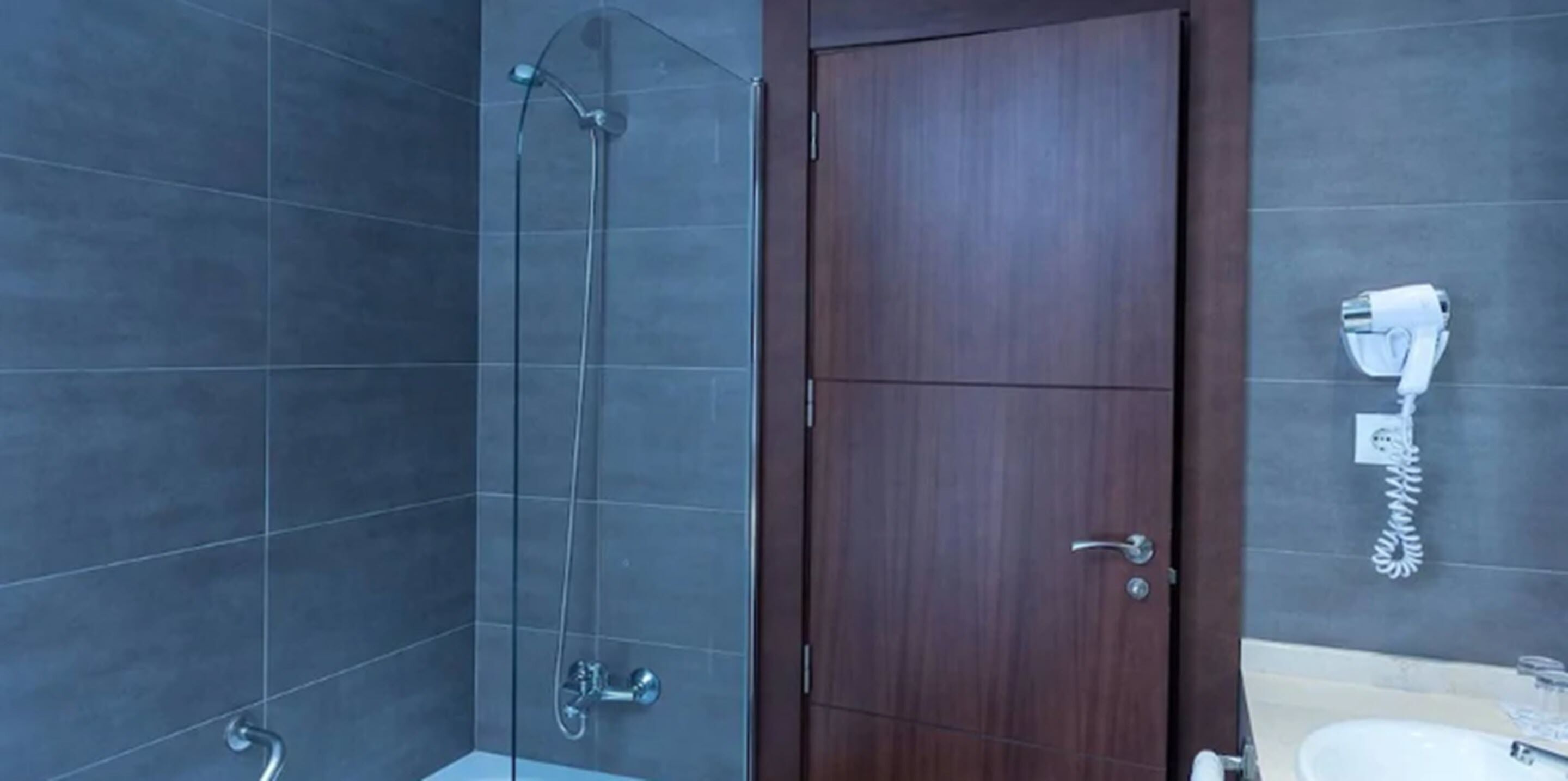 Un baño con cabina de ducha de vidrio, puerta de madera y dispensador de toallas en la pared.
