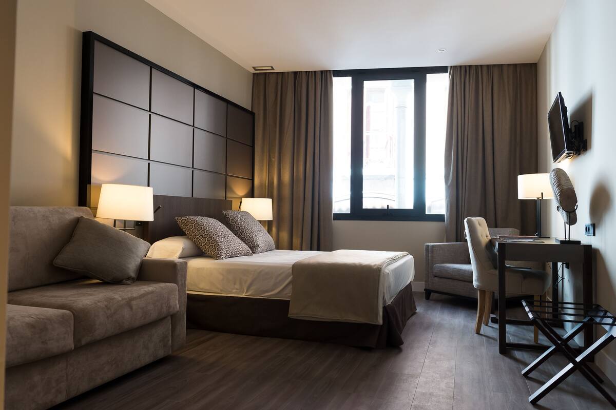 A hotel room with a bed, a sofa, a desk, and a chair.