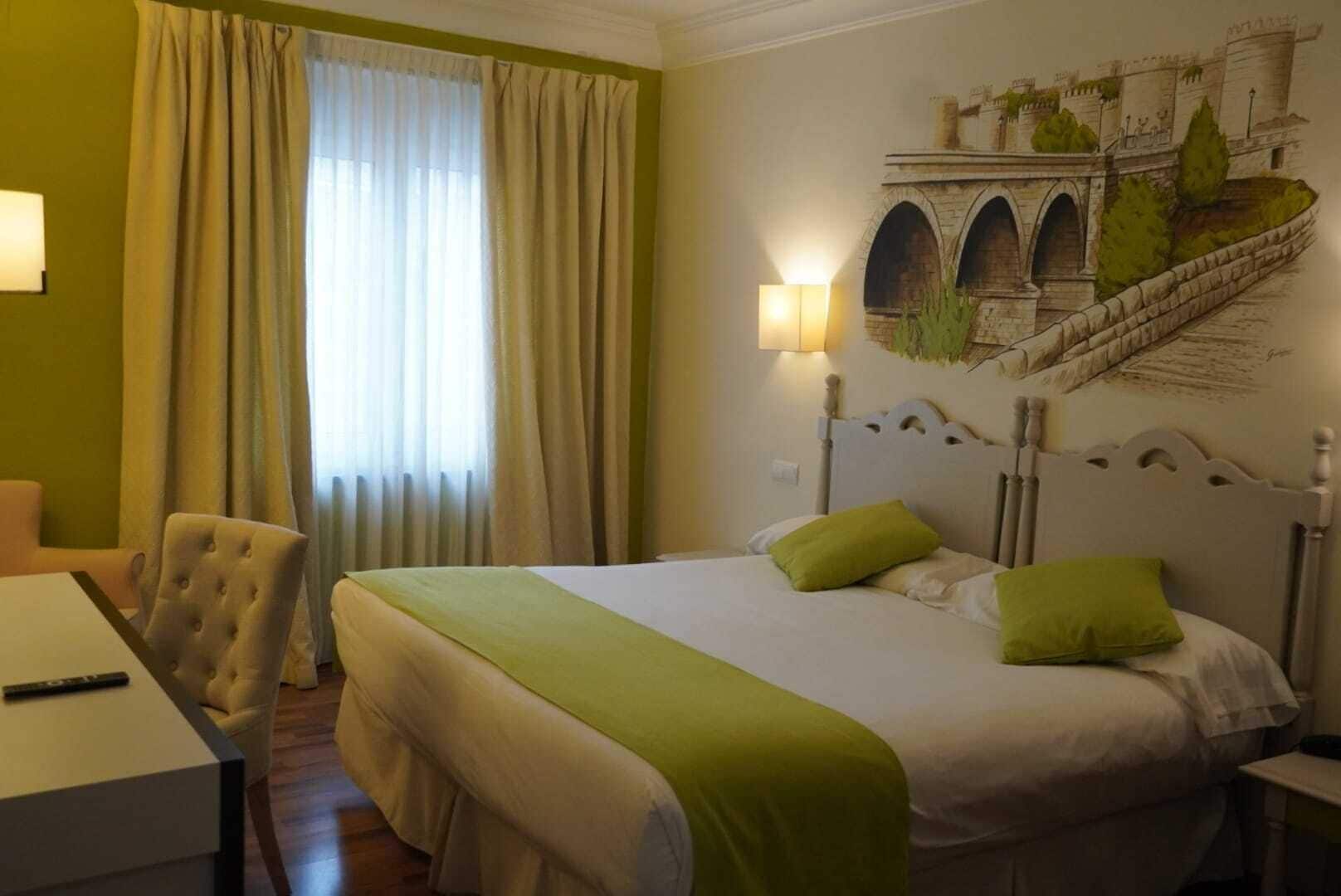 Habitació d'hotel amb un llit, una cadira, un escriptori i un mural d'un pont.