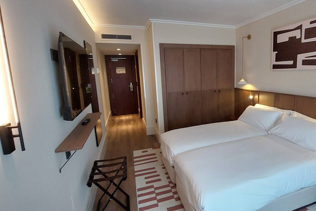 A hotel room with a bed, bedside table, lamp, and a mirror on the wall.