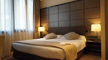 A hotel room with a large bed, two bedside lamps, a headboard with a grid pattern, and a window with curtains.