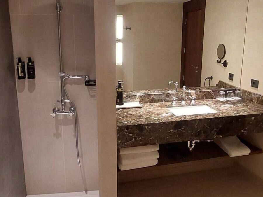 Ein modernes Badezimmer mit Dusche, Waschbecken und Marmorplatte sowie einem Spiegel.