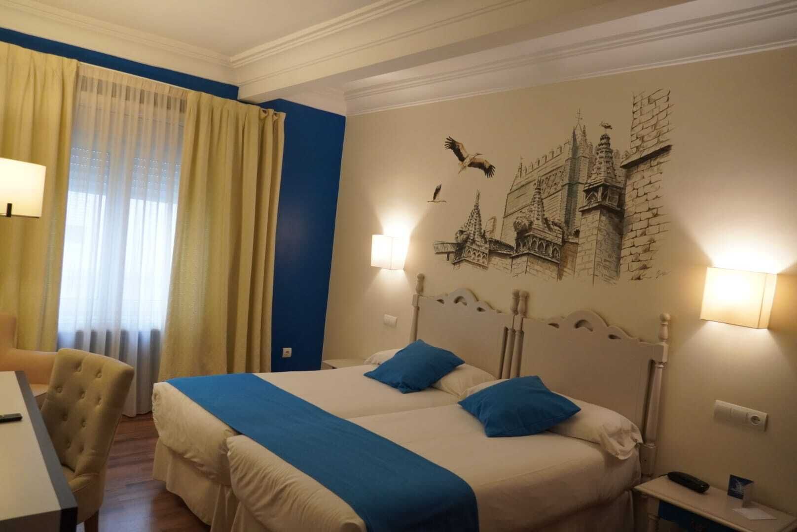 Ein Hotelzimmer mit einem großen Bett, zwei Kissen, einem Schreibtisch, einem Sessel und einem Wandbild.
