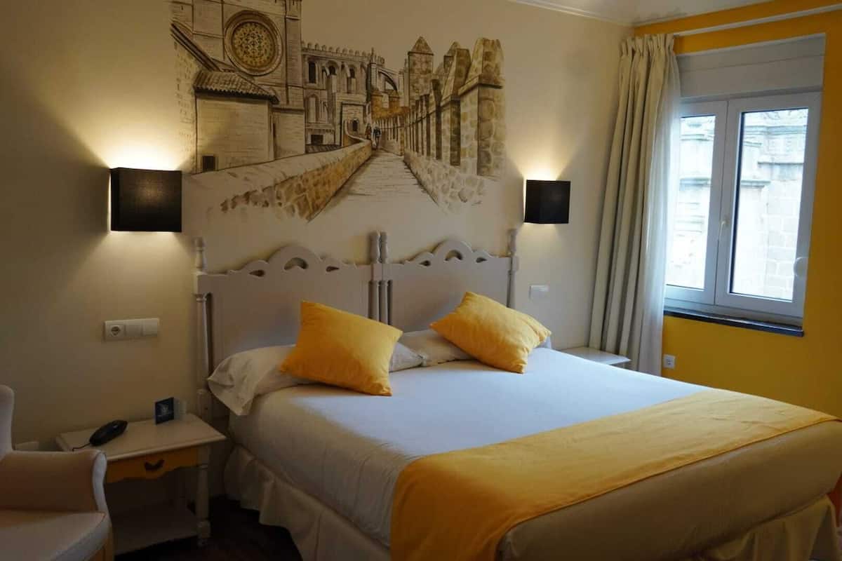 A hotel room with a bed, a nightstand, a chair, a wall mural, and a window.
