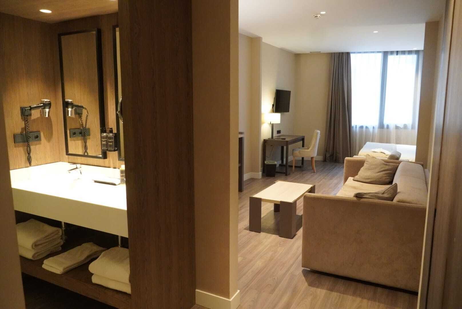 A hotel room with a large mirror, a sofa, a small table, and a TV.