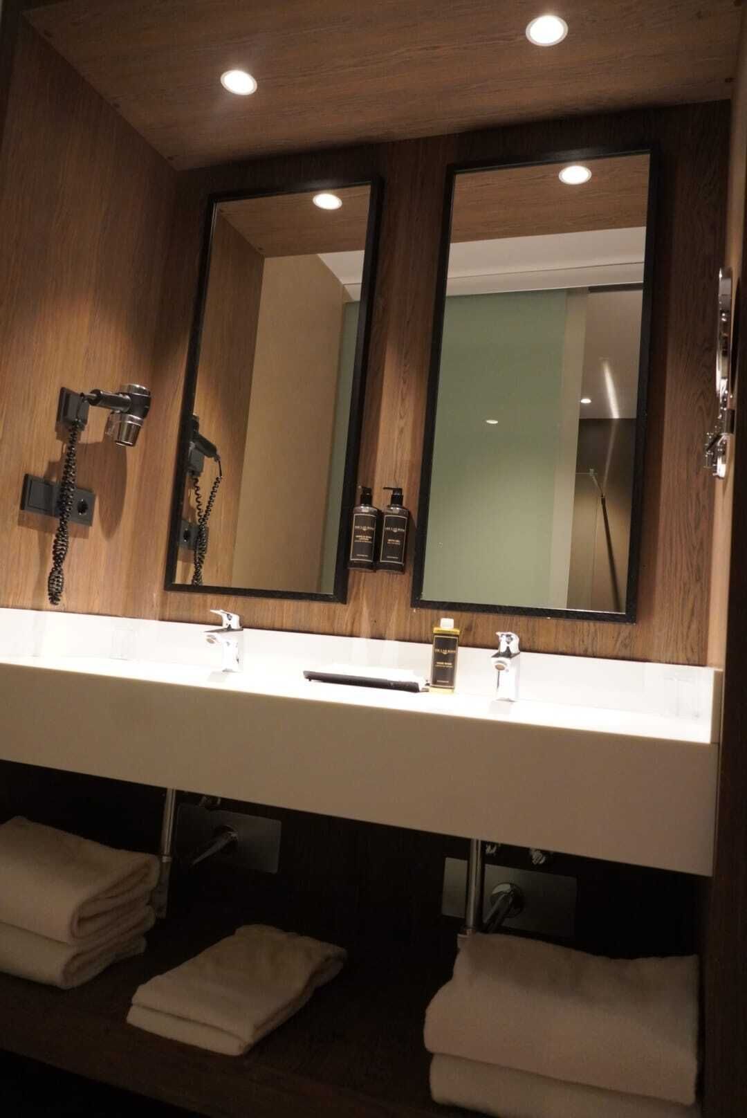 Une salle de bain d’hôtel avec deux lavabos, un miroir, un sèche-cheveux et des serviettes.