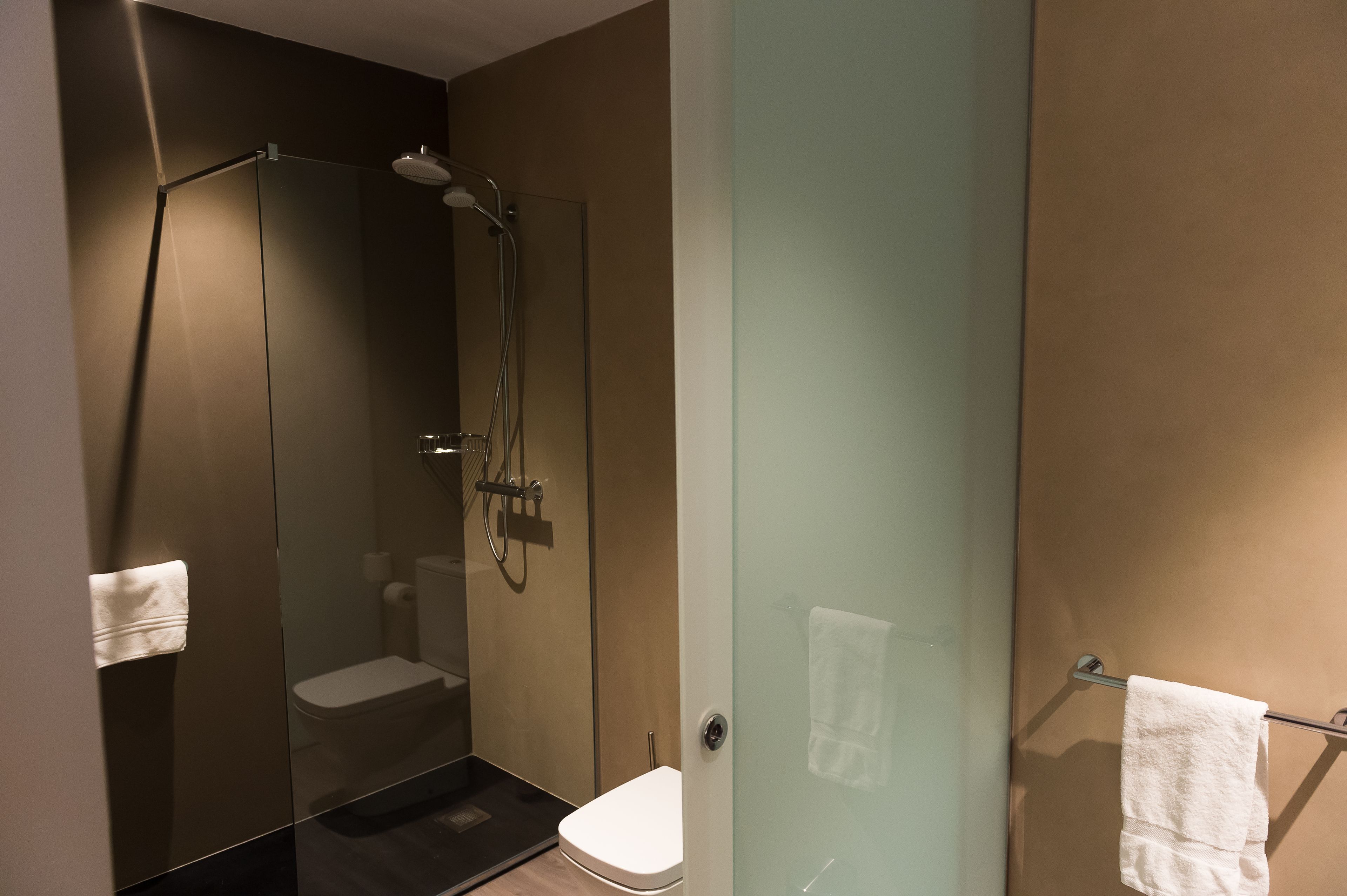 A modern bathroom with a glass-enclosed shower, a toilet, and a towel rack.