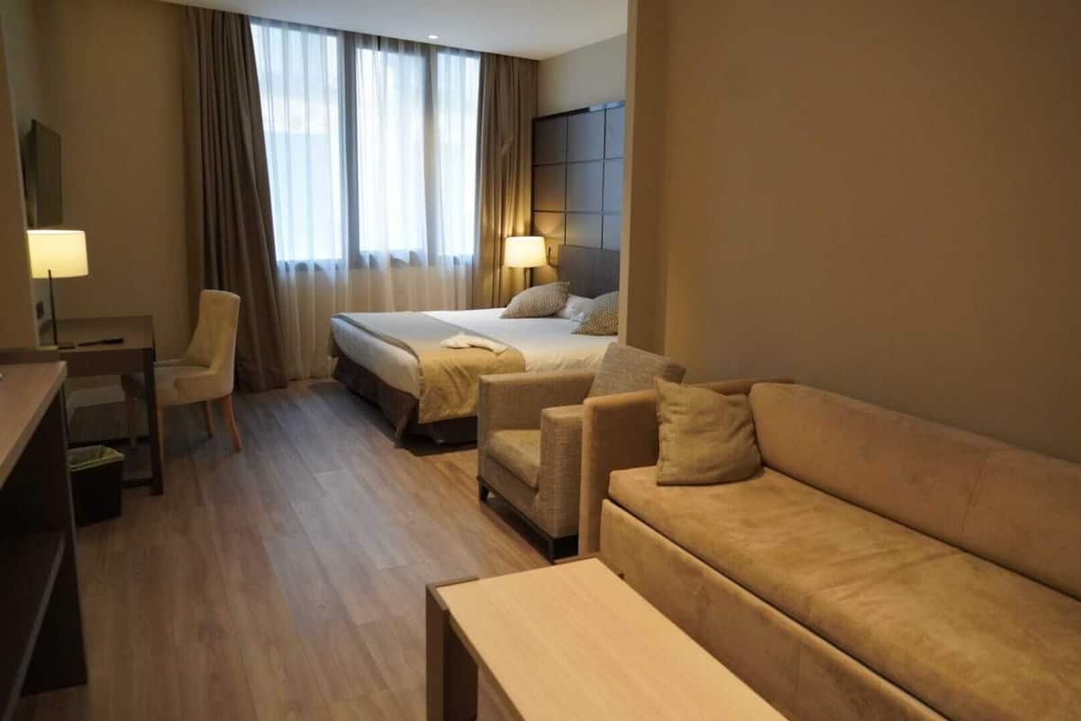 A hotel room with a bed, two armchairs, a sofa, a desk, and a lamp.
