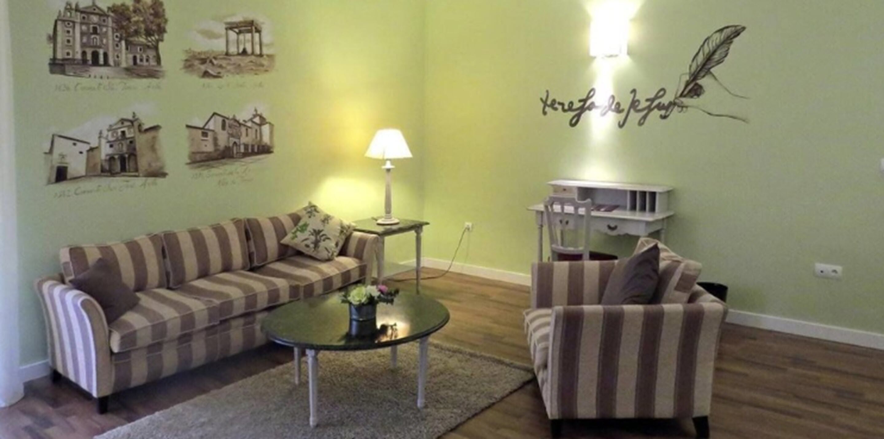 A living room with striped sofas, a glass coffee table, a lamp, and wall art depicting buildings.