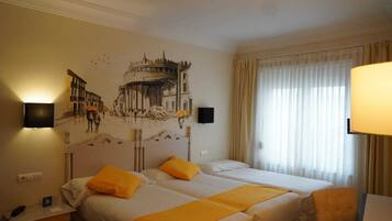 A hotel room with two beds, a mural on the wall, a desk with a lamp, and a window with curtains.