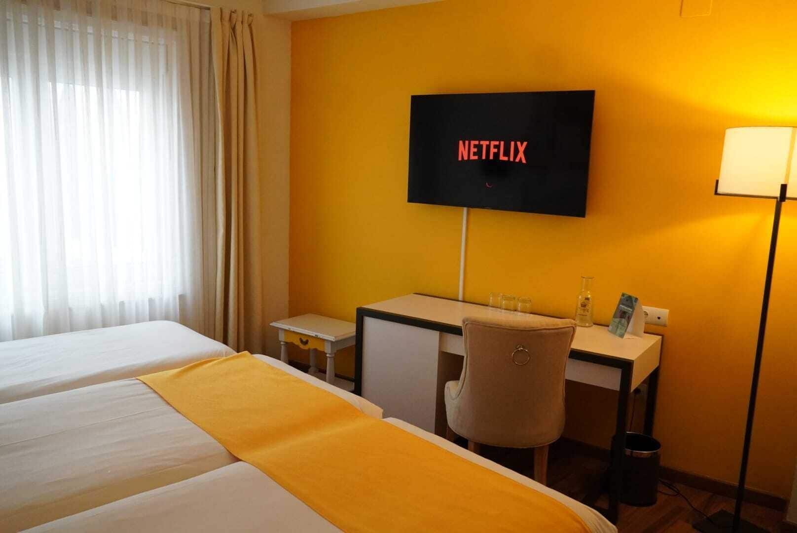 Habitación de hotel con cama, escritorio, silla, televisor montado en la pared y lámpara.