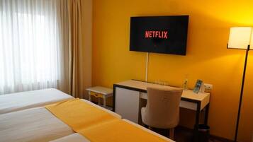 Habitación de hotel con cama, escritorio, silla, televisor montado en la pared y lámpara.