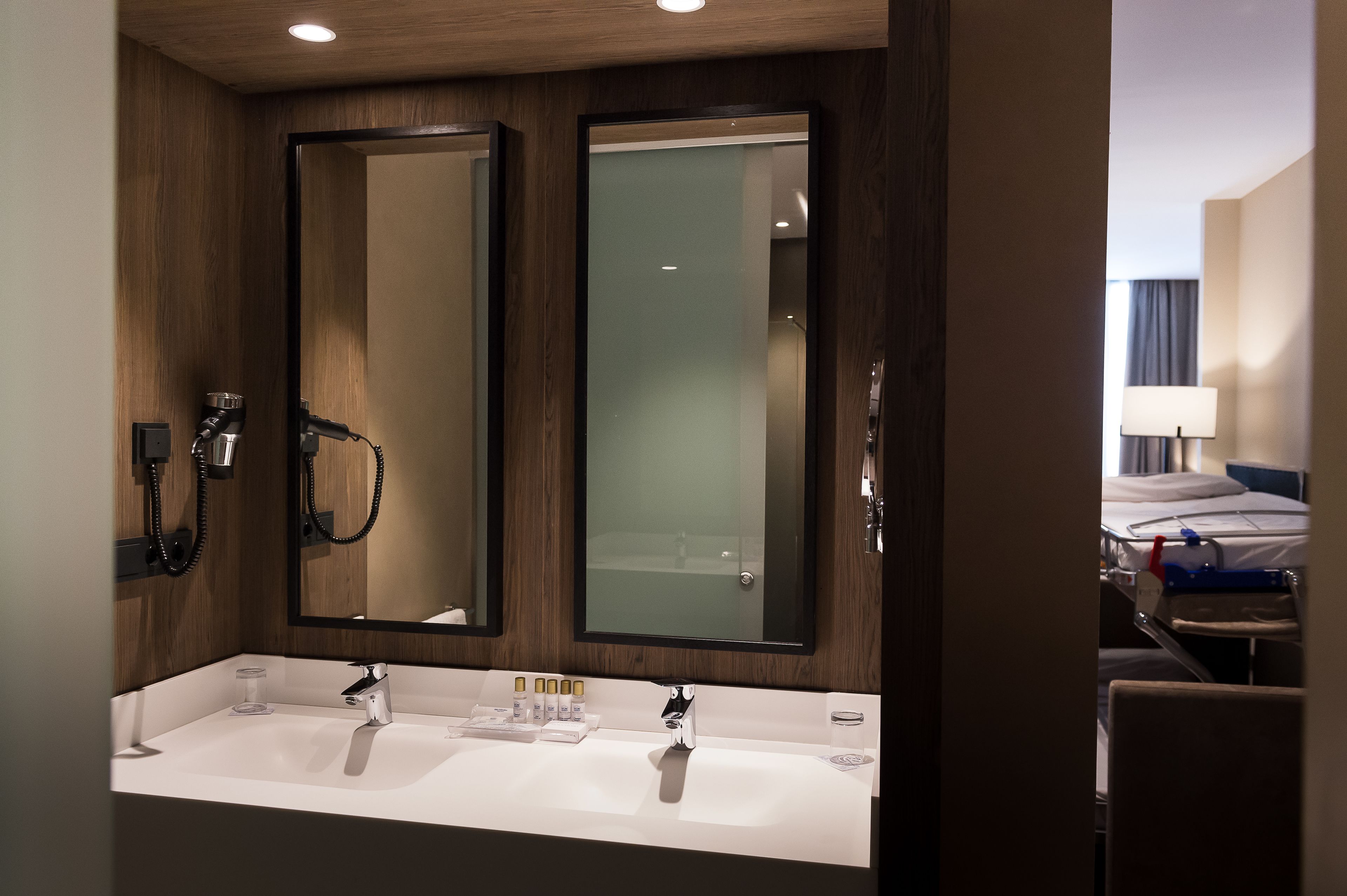 A hotel bathroom with two sinks, a large mirror, and a shower area.