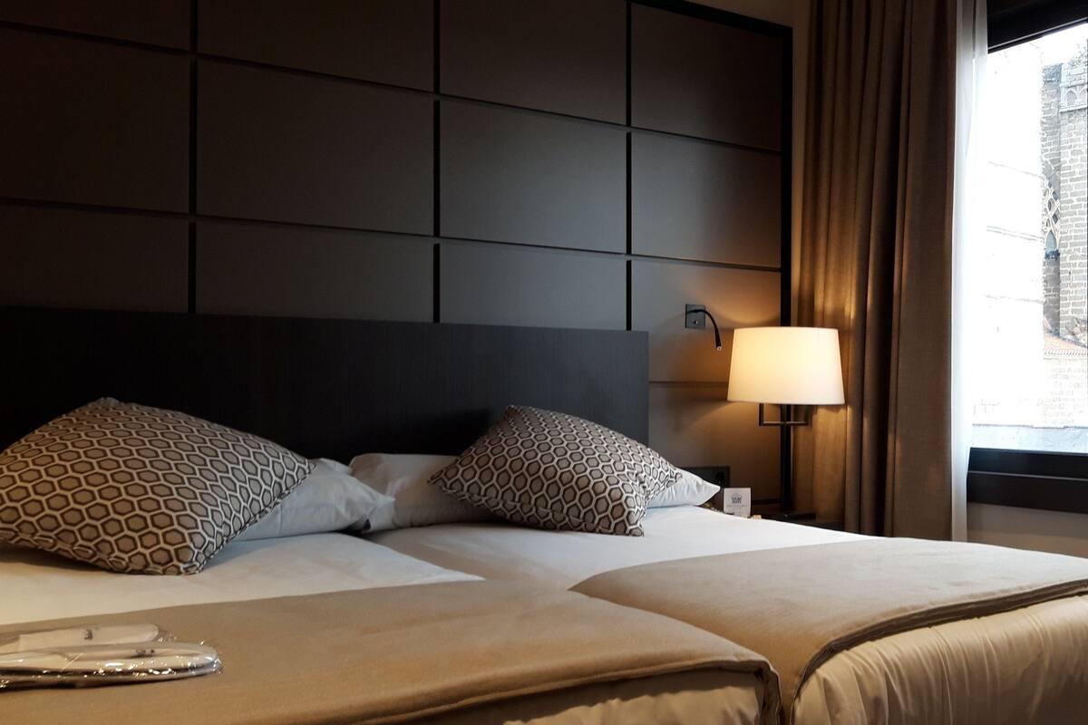 A hotel room with a large bed, a bedside lamp, and a view of a historic building through the window.
