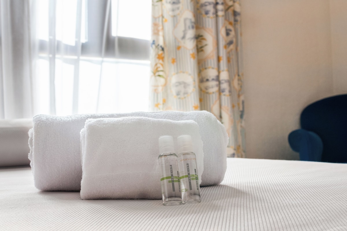 A neatly made bed with rolled white towels and two small bottles of toiletries.