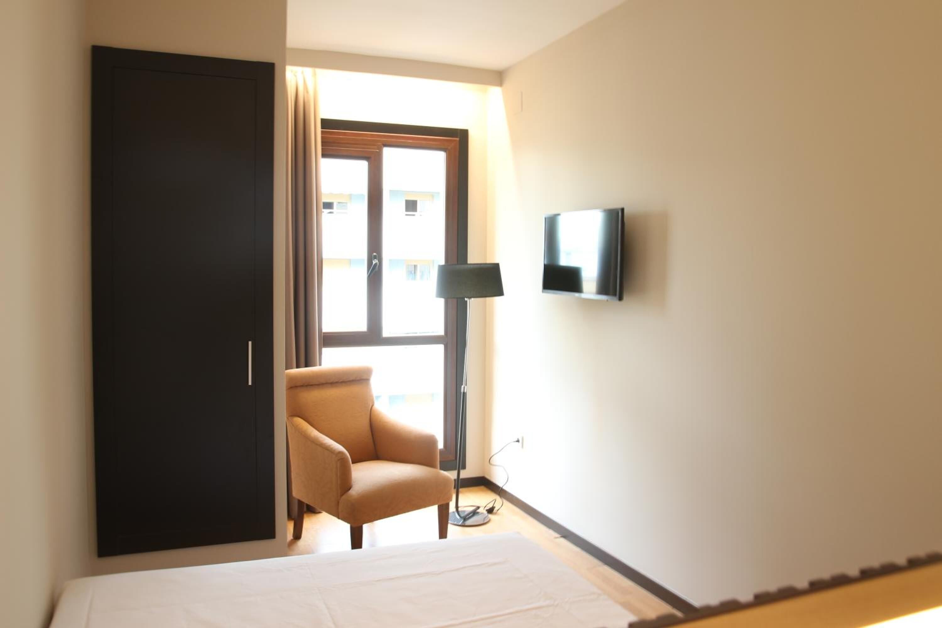 A hotel room with a bed, a chair, a TV, and a wardrobe.