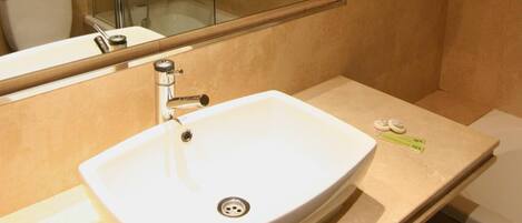 A bathroom with a large mirror, a white sink, a glass shower enclosure, and a towel rack with towels.