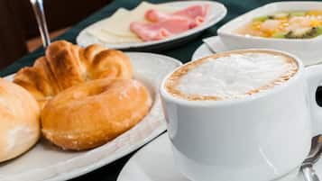A breakfast setting with croissants, a cup of coffee, and plates of ham and fruit.