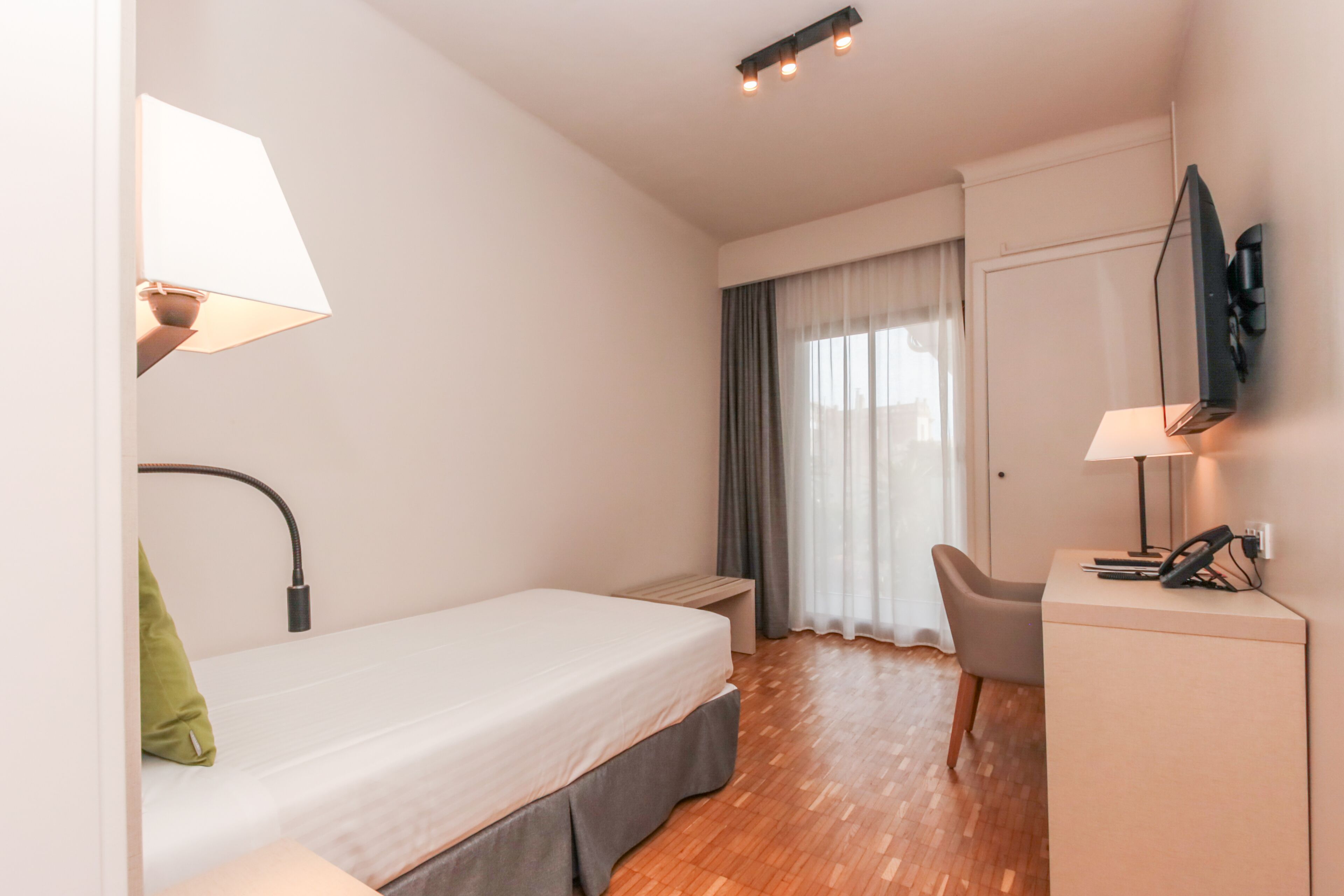 Ein Hotelzimmer mit einem Bett, einem Schreibtisch, einem Sessel, einem Fernseher und einem Vorhangfenster.