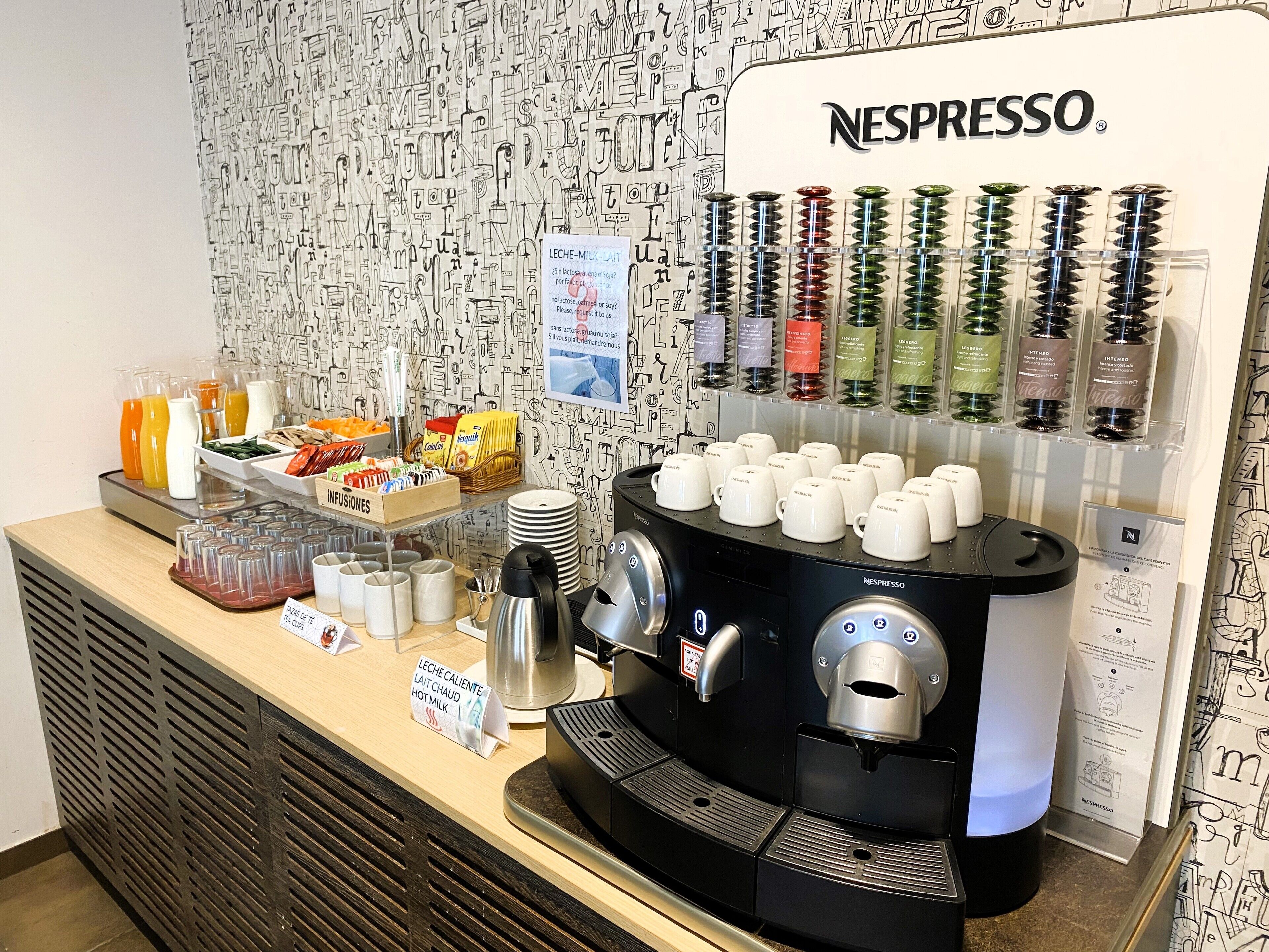 Una estación de café Nespresso con varios dispensadores, diferentes opciones de leche y una selección de bebidas.