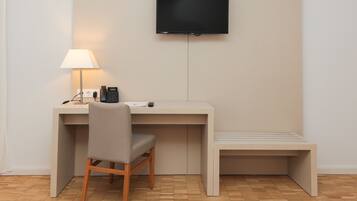 A modern hotel room with a desk, chair, lamp, phone, and a flat-screen TV mounted on the wall.