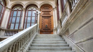 Een statige trap met versierde balustrades die naar een houten deur met ingewikkelde snijwerken leidt.