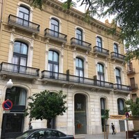 Un edificio a più piani con balconi decorati, un ampio ingresso ad arco e una vetrina con insegne.