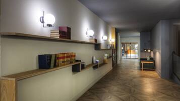 A hallway with wooden shelves, books, and wall-mounted lights.
