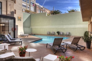 A rooftop pool area with lounge chairs and a small table, surrounded by buildings. - Hotel Lauria (Tarragona)