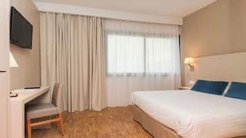 A hotel room with a bed, a desk, a chair, a television, and a window with curtains.