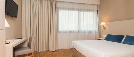 Une chambre d’hôtel équipée d’un lit, d’un bureau, d’une chaise, d’une télévision et d’une fenêtre avec des rideaux.
