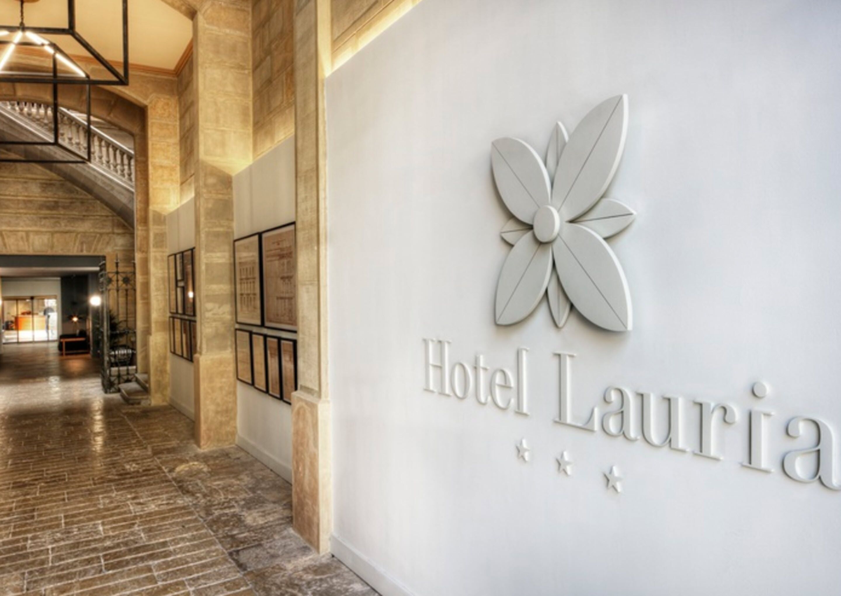 A hotel entrance with a modern design, featuring a large flower logo and the name 'Hotel Lauria' on the wall.