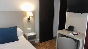 Una habitación de hotel con una cama, un escritorio, una silla, una lámpara de escritorio, un teléfono y una televisión.