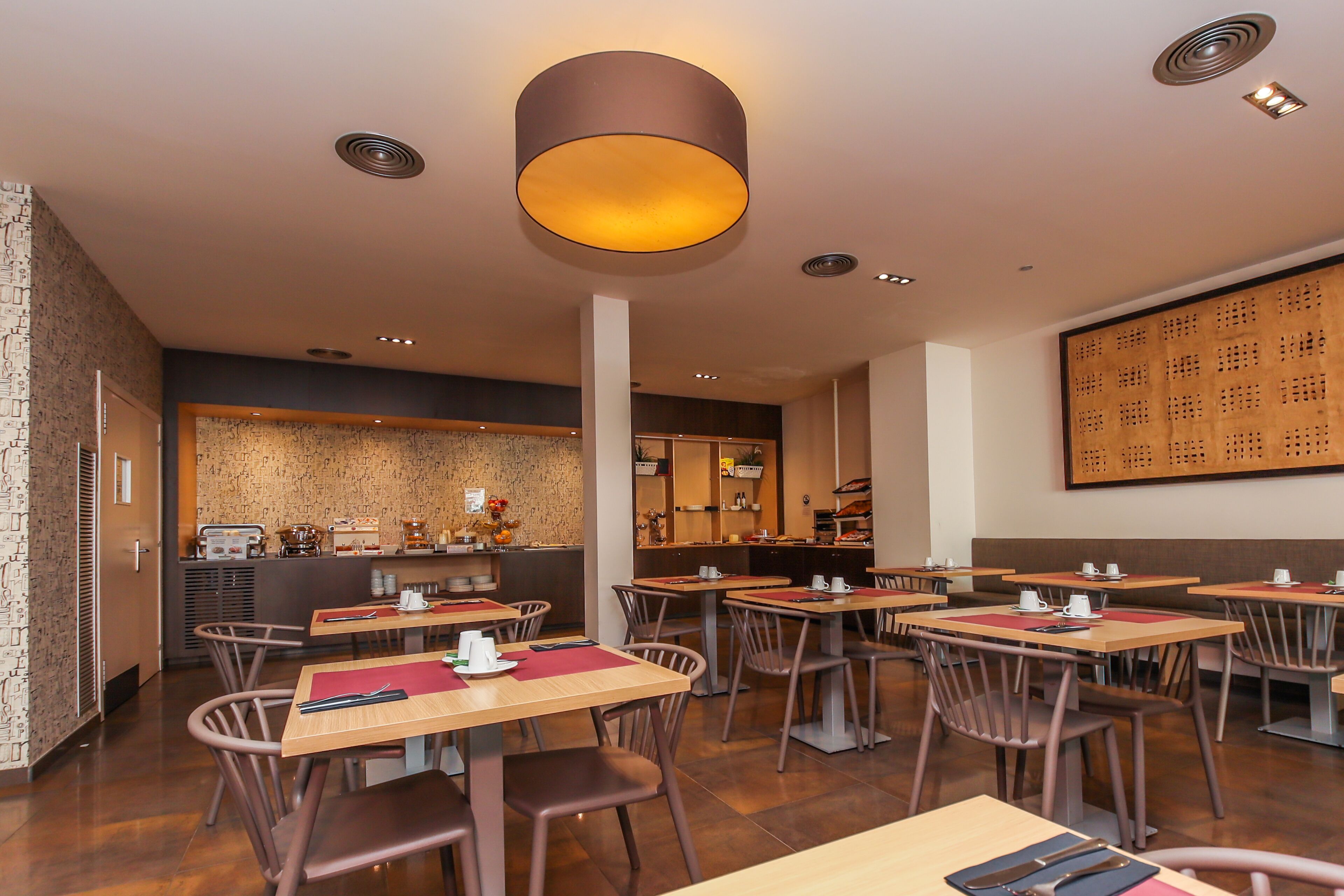 A restaurant with multiple tables and chairs, a counter with a coffee machine, and a large wall with a patterned design.