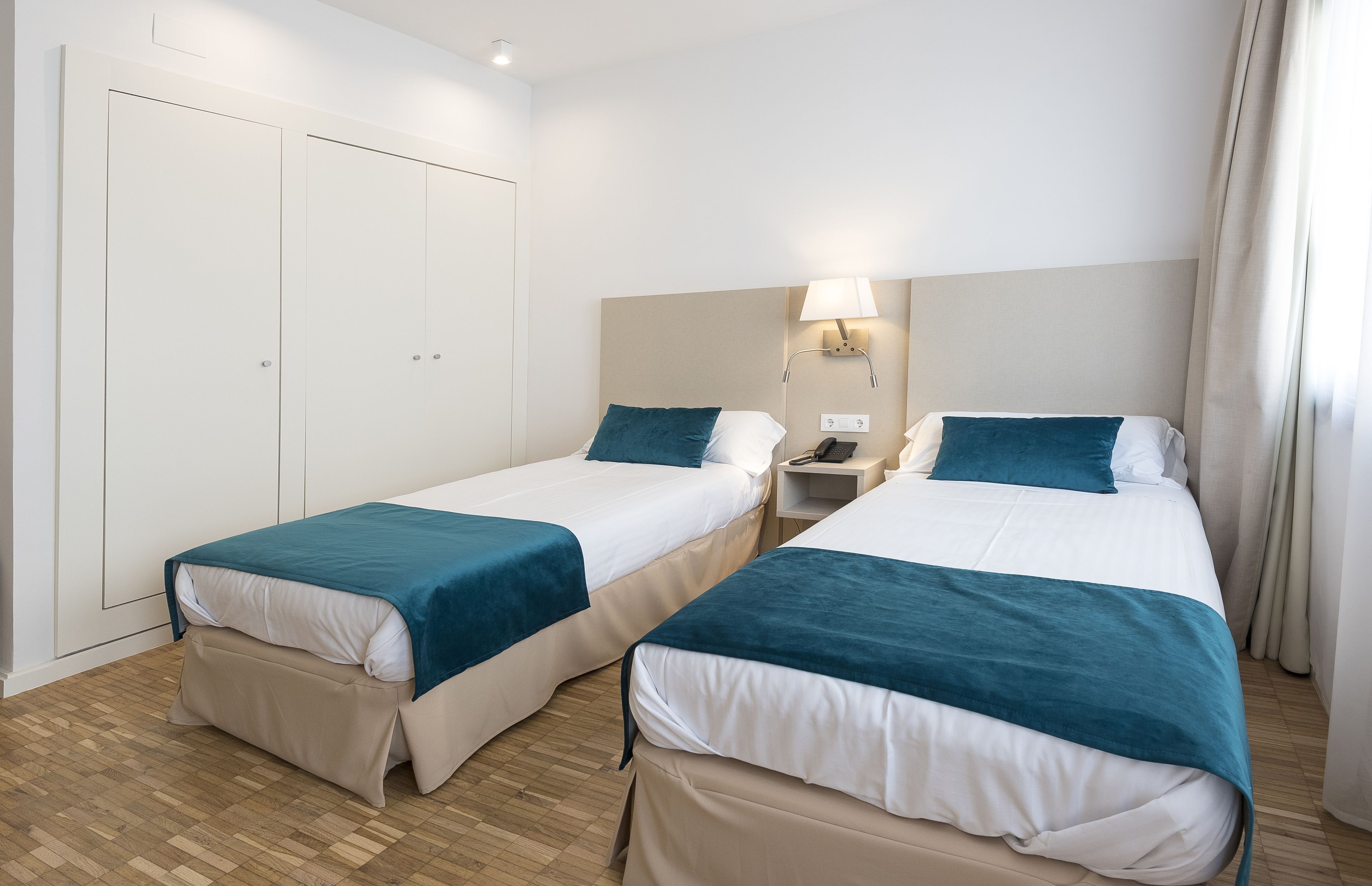 A hotel room with two single beds, a wardrobe, a bedside table with a lamp, and a telephone.