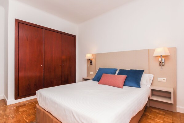 A bedroom with a large wooden wardrobe, a bed with white and blue bedding, and bedside lamps.