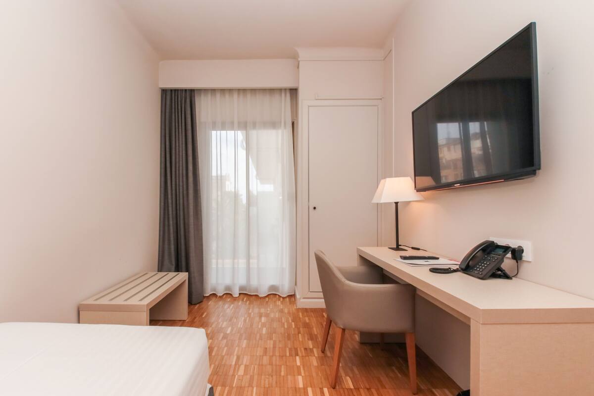 Habitación de hotel con cama, escritorio, silla, televisor, lámpara y teléfono.